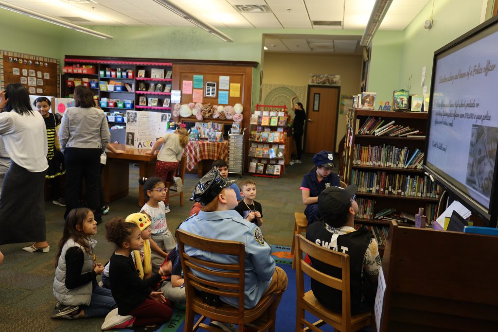 Children sit in a group around a presentation