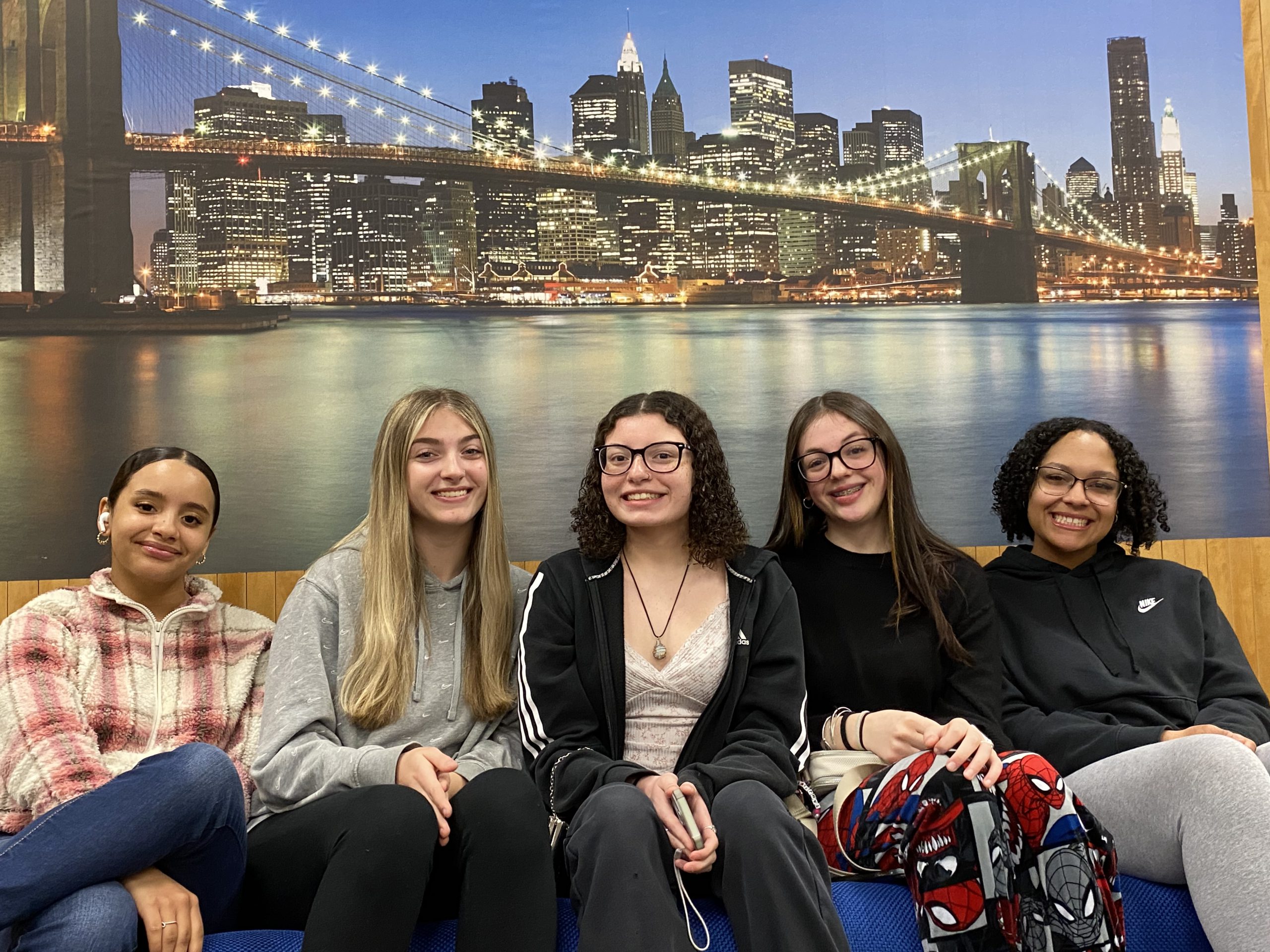 Five female students pose in front of a mural of NYC